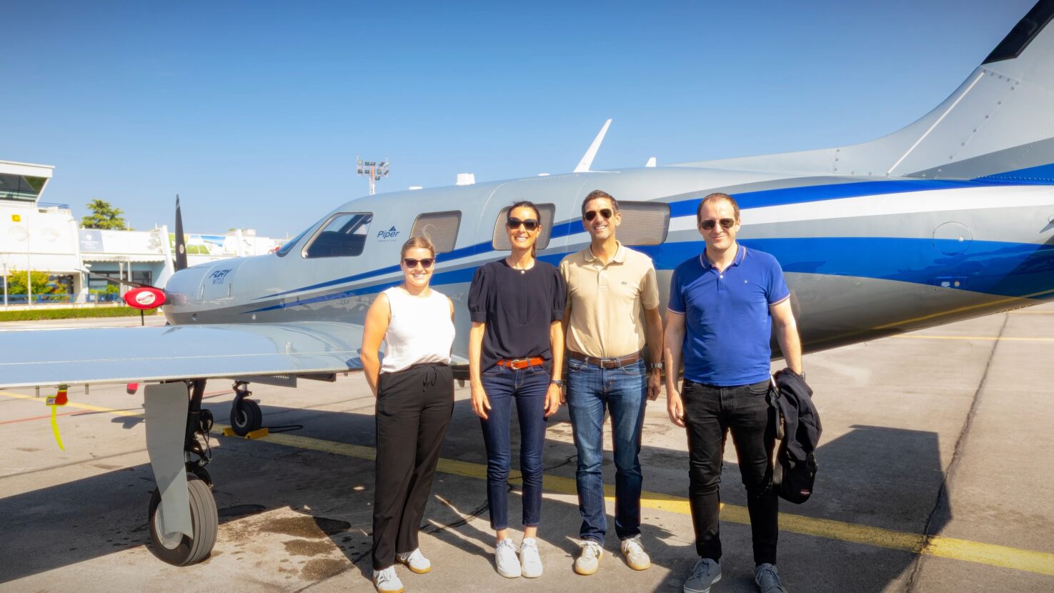 Four Piper European Fly-In attendees stand in front of a blue-and-silver Piper M700 Fury at Portorož Airport.